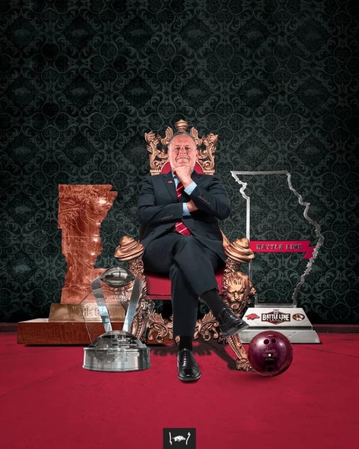 Sam Pittman sits on a throne surrounded by all the trophies his Razorbacks won in 2021, along with Larry the Bowling Ball.